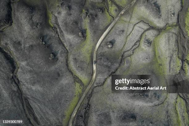 drone image looking down on a 4x4 driving along a dirt road crossing a volcanic landscape, icelandic highlands, iceland - central highlands iceland stock pictures, royalty-free photos & images