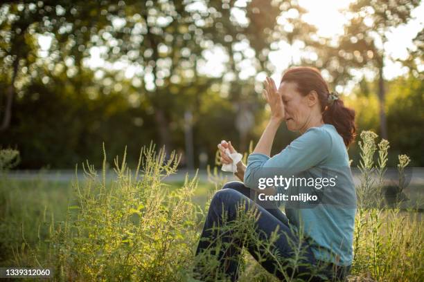 woman sitting outdoors and suffering from pollen allergy - allergie stockfoto's en -beelden