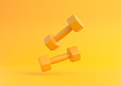 Two yellow rubber or plastic coated fitness dumbbells falling on yellow background