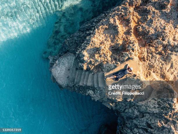 a woman is resting on a rock near a turquoise sea - palma maiorca 個照片及圖片檔
