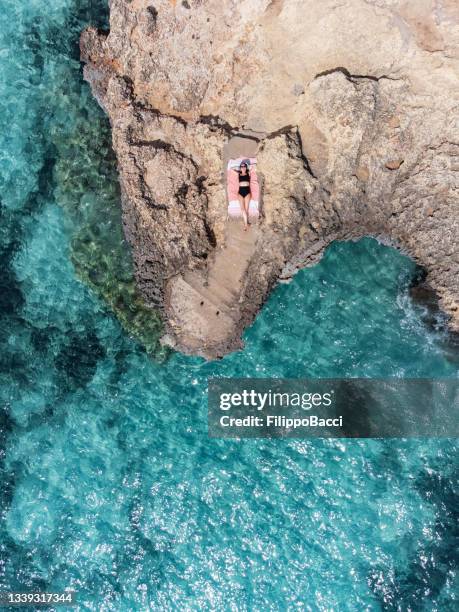 a woman is resting on a rock near a turquoise sea - palma mallorca stock pictures, royalty-free photos & images