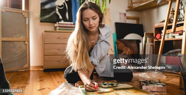 beautiful caucasian white woman drawing the picture in interior. working with paintbrush and paints. tablet and easel. warm atmosphere indoor. nice soft light around - amateur stock pictures, royalty-free photos & images