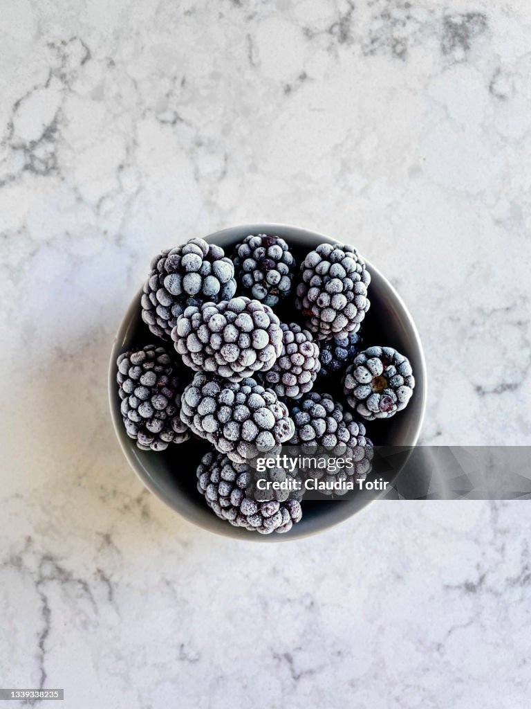 Frozen blackberries in a bowl on white, marble background