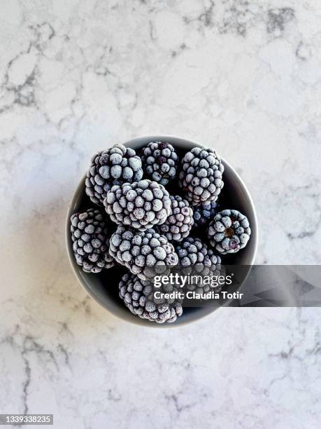 frozen blackberries in a bowl on white, marble background - brombeere und himbeere stock-fotos und bilder