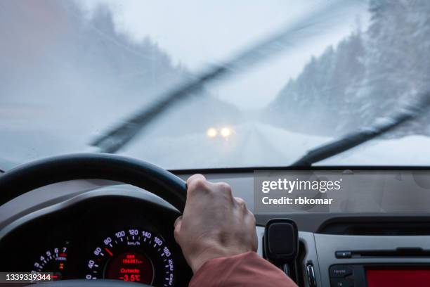 view through the windshield of a car driving on a snow covered rural highway during a winter blizzard snowstorm in forest - schneeregen stock-fotos und bilder