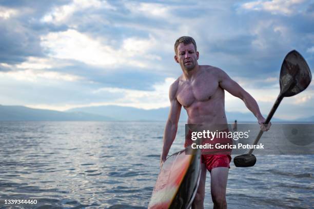handsome young man prepares to paddle kayak on mountain lake - muscle men at beach stock pictures, royalty-free photos & images