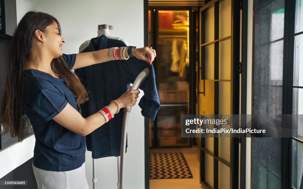 Young newlywed woman ironing cloth with garment steamer in her home.