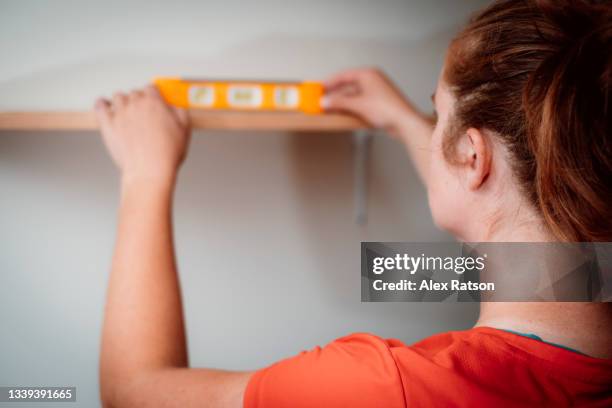 a women uses a level to place a diy shelf on the wall - building shelves stock pictures, royalty-free photos & images