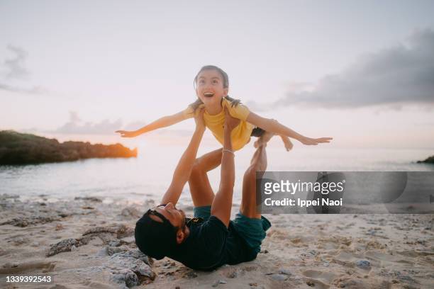 father and young daughter playing airplane on beach at sunset - candid beach stock-fotos und bilder