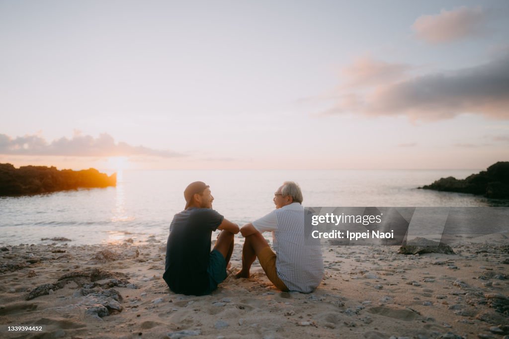 Senior father and adult son having a good time on beach at sunset