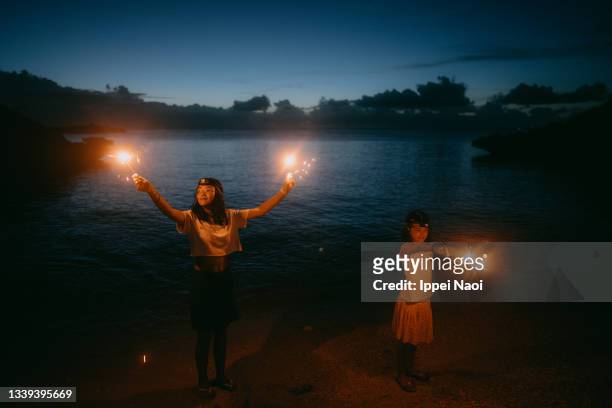 two cheerful sisters playing with sparklers on beach at night - japan 12 years girl stock pictures, royalty-free photos & images