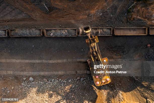aerial view of open pit iron ore and heavy mining equipment. large excavator loads iron ore into train carriages - mina de superficie fotografías e imágenes de stock