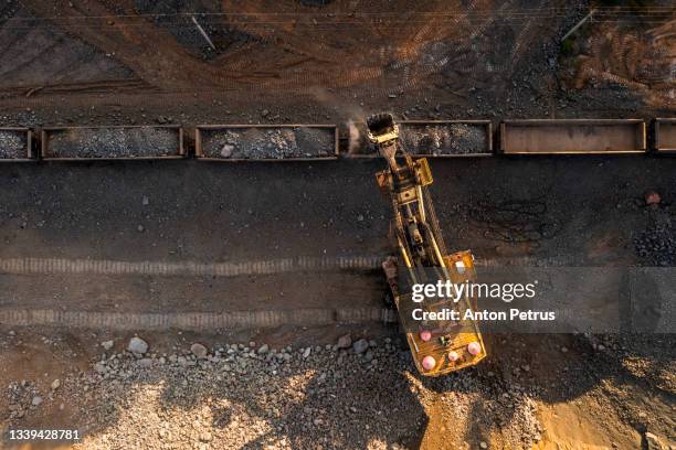 aerial view of open pit iron ore and heavy mining equipment. large excavator loads iron ore into train carriages - copper mine stock pictures, royalty-free photos & images
