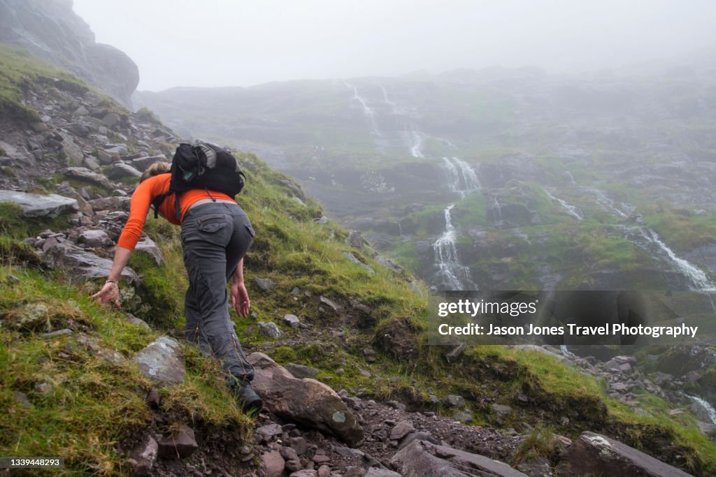 A woman with backpack climbs up near waterfalls on Carrauntoohil in Kerry