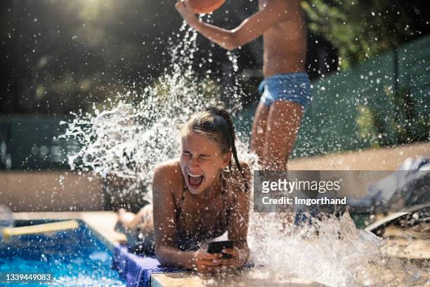 teenager, der seine schwester mit einem eimer wasser bespritzt - girl wet stock-fotos und bilder