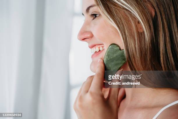 skin care woman skin care using gua sha  stone - facial massage stock pictures, royalty-free photos & images