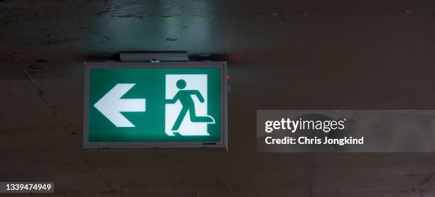 emergency exit sign hanging from ceiling in dark room - emergency exit light stock pictures, royalty-free photos & images