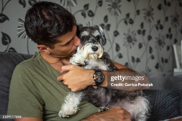 young man kissing his schnauzer dog at home - schnauzer stock pictures, royalty-free photos & images