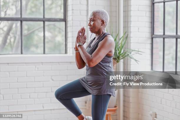 femme âgée active faisant du yoga à la maison - équilibre photos et images de collection