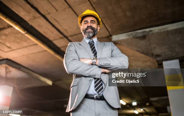 mature architect standing at new public car garage and looking at camera. - person in suit construction stock pictures, royalty-free photos & images