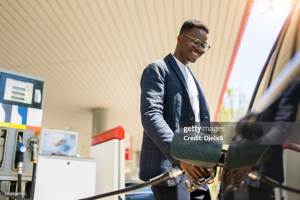 Feliz joven afroamericano repostando su coche en la gasolinera.