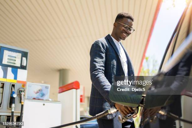 happy young african american man refueling his car the gas station. - bensinstation bildbanksfoton och bilder