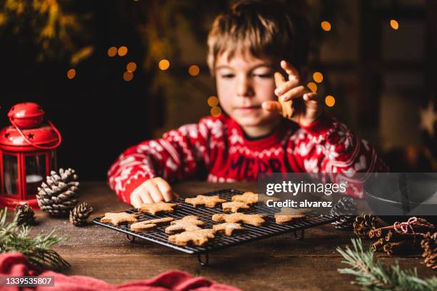 boy picking christmas cookie from cooling rack - kids cooking christmas stock pictures, royalty-free photos & images