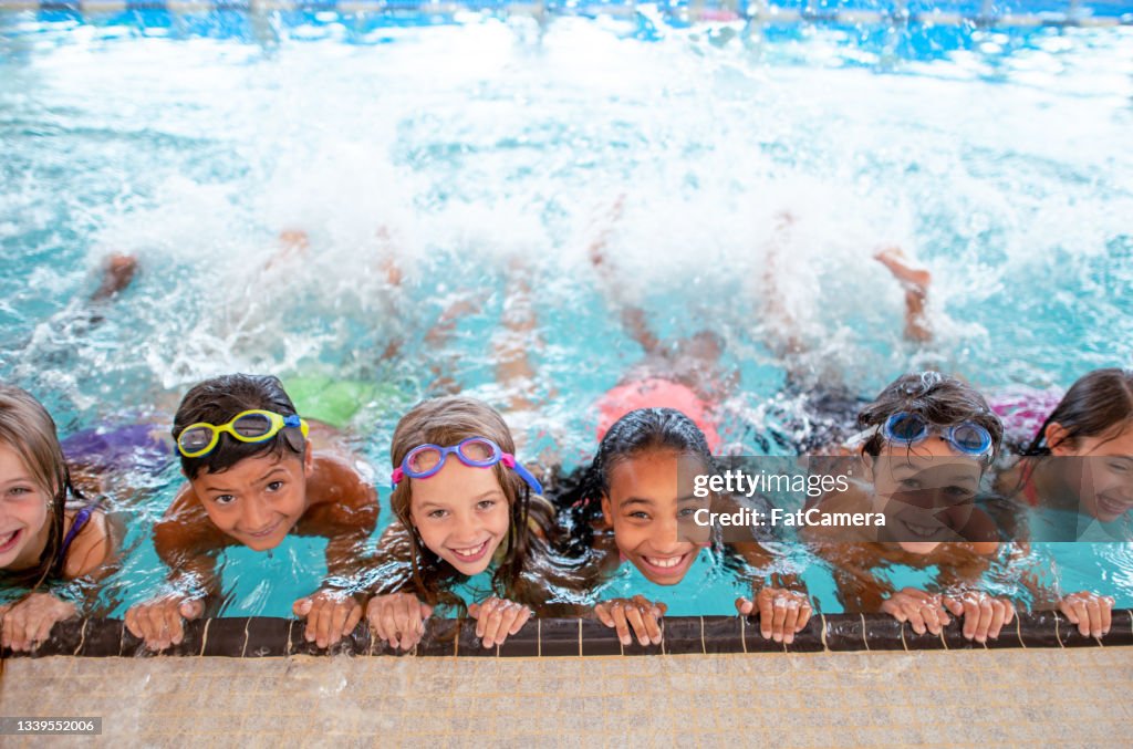 Multiethnische Gruppe von Kindern, die im Schwimmbad kicken lernen