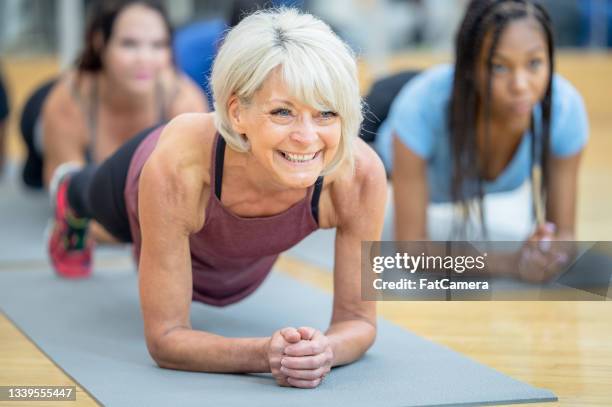 mujer mayor sonriente en pose de tablón durante la clase de ejercicios - clase de ejercicio fotografías e imágenes de stock