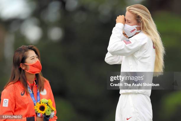 Silver medalist Mone Inami of Team Japan watches gold medalist Nelly Korda of Team United States wearing a mask on the podium at the medal ceremony...