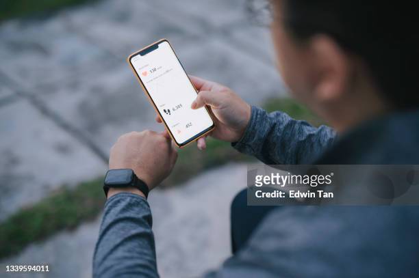 over shoulder view asian chinese man using fitness tracker mobile app connecting to fitness tracker at public park after exercise in the morning - holding stock pictures, royalty-free photos & images
