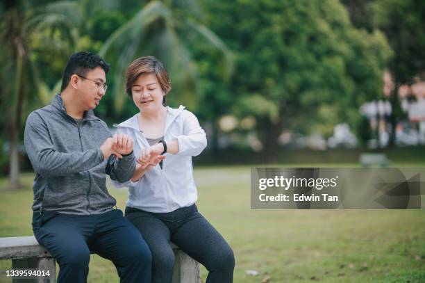 pareja asiática china de adultos medios que usa la aplicación móvil fitness tracker que se conecta al rastreador de fitness en el parque público después del ejercicio por la mañana en el banco del parque - checking sports fotografías e imágenes de stock