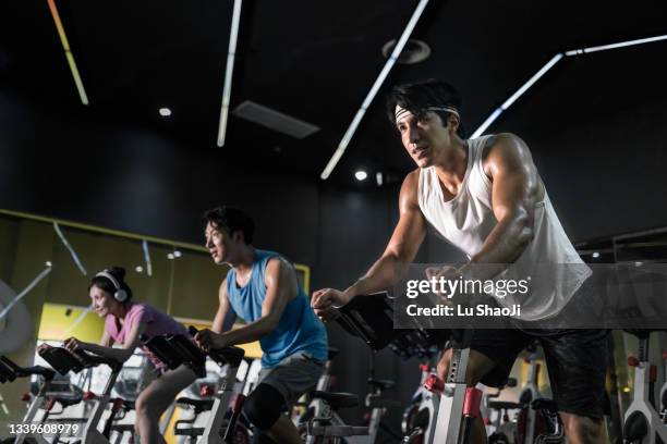 young people riding stationary bike during indoor cycling class in gym. - exercise bike fotografías e imágenes de stock