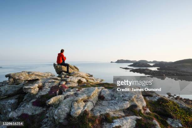 man sitting on gweal hill looking across hell bay towards shipman head on the island of bryher. - isles of scilly stock pictures, royalty-free photos & images