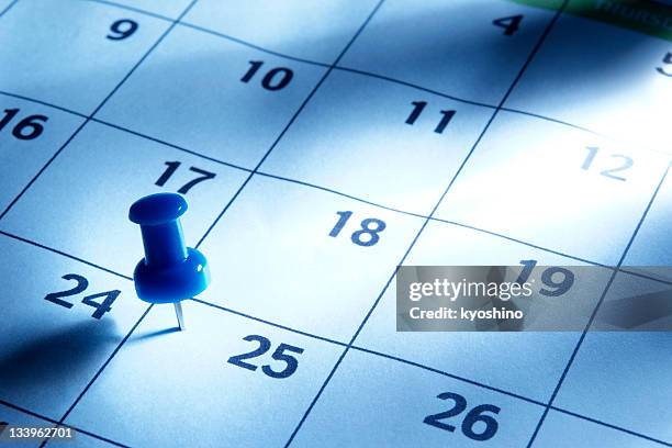 blue tinted image of thumbtack in calendar with light rays - calendar concept stockfoto's en -beelden