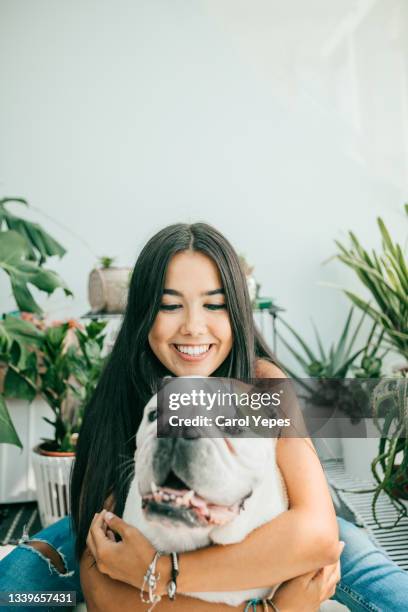 latina young woman petting dog at home in domestic environmnet - petite latina fotografías e imágenes de stock