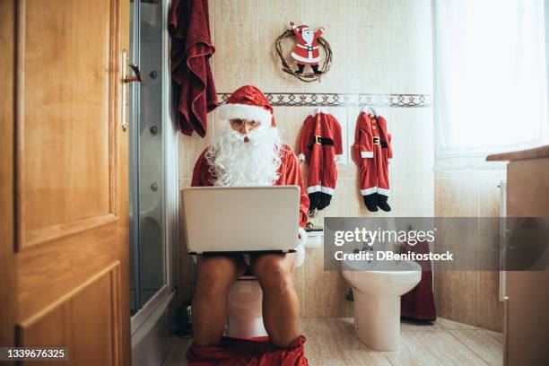 santa claus at christmas, in his bathroom, sitting on the toilet, working with the laptop - komiek stockfoto's en -beelden