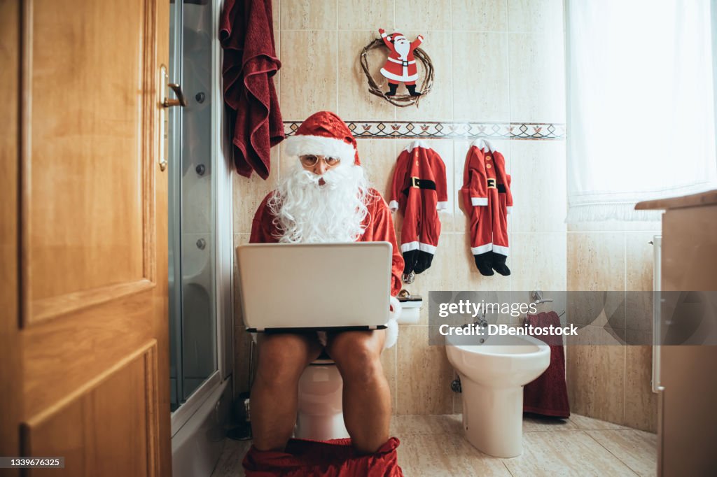 Santa Claus at Christmas, in his bathroom, sitting on the toilet, working with the laptop