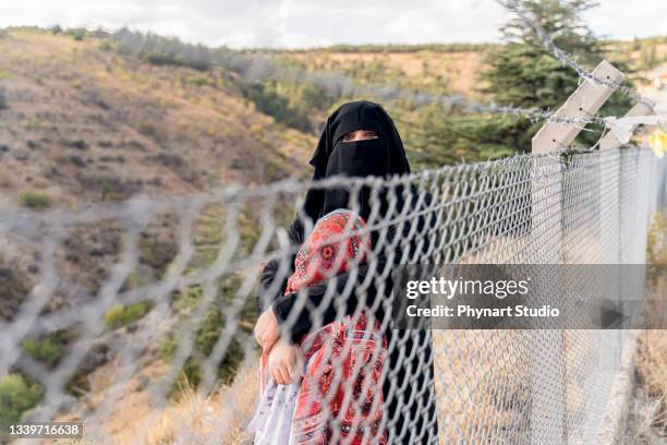 refugee woman and daughter standing behind a fence - runaway stock pictures, royalty-free photos & images