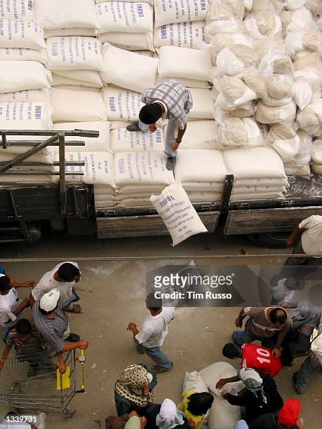 United Nations Relief and Works Agency worker tosses bags of wheat flour to Palestinian refugees August 17, 2002 in Dheishen refugee camp, West Bank....