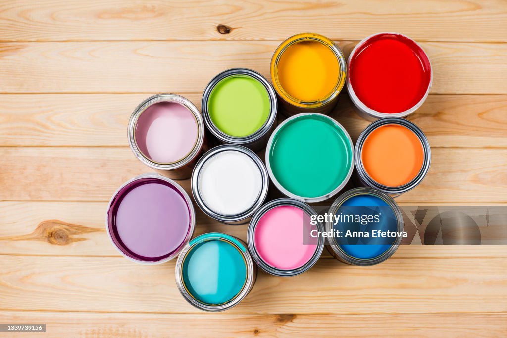 Set of open metal buckets with bright multicolored paints ready for renovation works on timber floor. Flat lay style. Copy space for your design. Concept of redecoration in home interior. Color swatch for design ideas