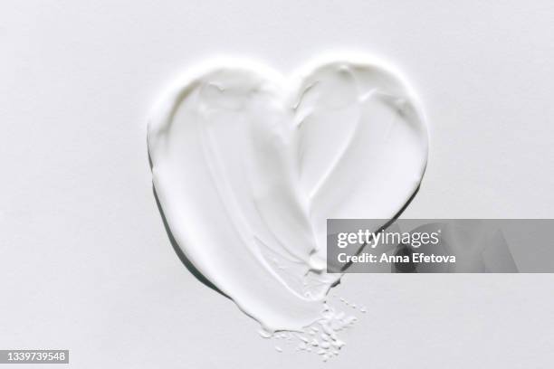 textured smears of white cream applied on white background in heart shape. body lotion for perfect skin. macrophotography in flat lay style - cremefarbig stock-fotos und bilder