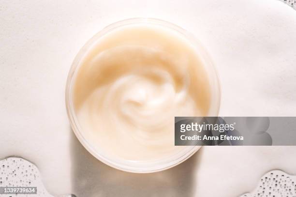 glass jar with beige cream on white foam. concept of body care and beauty. flat lay style and close-up - cosmetic jar stockfoto's en -beelden