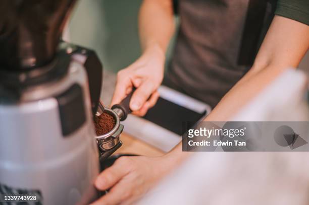 hochwinkel asiatischer chinesischer barista-mann mahlen und stopfen von gemahlenem kaffee mit einem tamper-siebträger mit kaffeemahlmaschine - coffee grinder stock-fotos und bilder