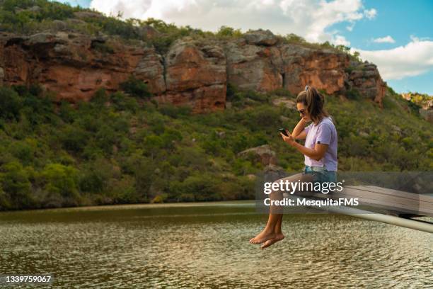 woman using smartphone sitting pier river bank - brazil global tour stock pictures, royalty-free photos & images