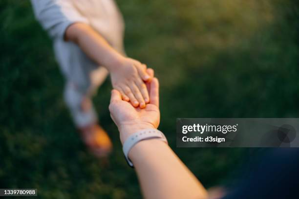 close up of mother holding hand of little daughter on lawn, relaxing and enjoying family bonding time on a lovely day in park. family love and care. connection with nature concept - chinese mothers day foto e immagini stock