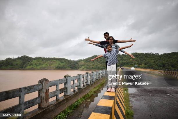 family with arms stretched standing on a  bridge surrounded by a serene lake - enjoy monsoon stock-fotos und bilder