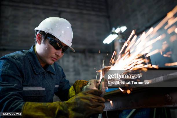 industrial worker in a factory with electric grinder tools to cut a metal workpiece. - ferronnerie photos et images de collection