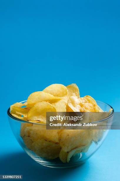 crispy fried fatty potato chips in a glass bowl or plate, on a blue background or table. the concept of unhealthy diet and lifestyle, the accumulation of excess weight. a copy of the text space. - bag of chips fotografías e imágenes de stock