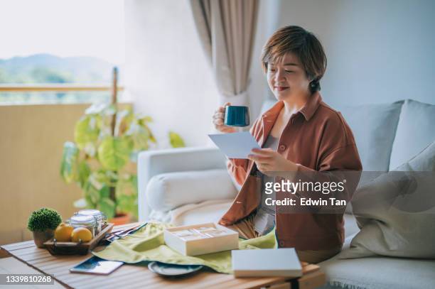 asian chinese mid adult woman unwrapping mooncake gift box reading greeting card at living room - care package stock pictures, royalty-free photos & images
